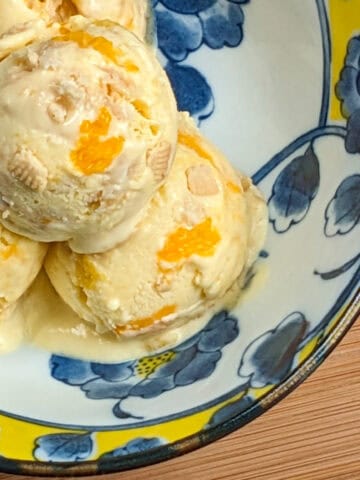 Mango cookies and cream ice cream served in a vibrant floral bowl on a wooden surface.